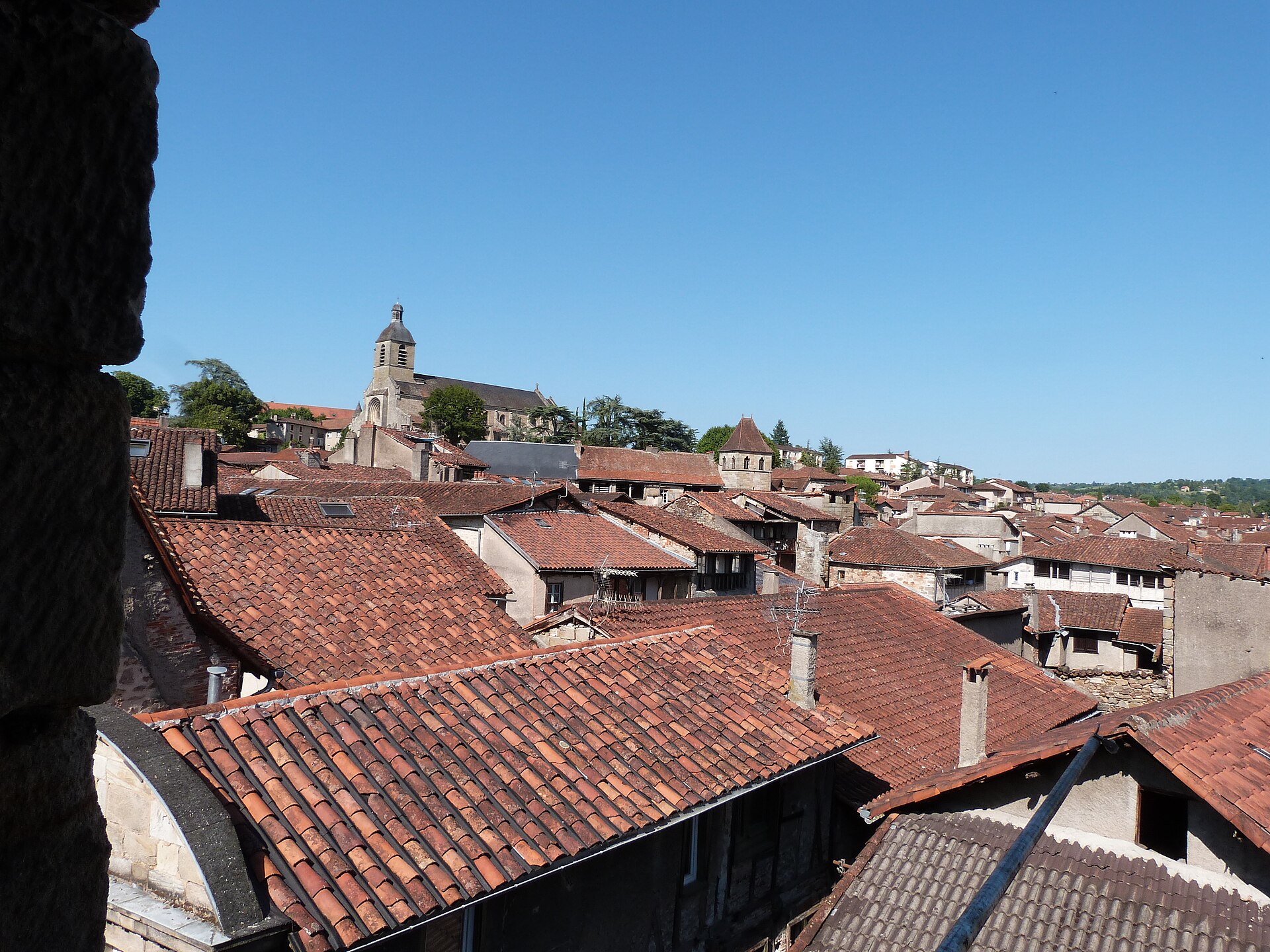 Toits de tuiles rouges d’une ville moyenne dominés par un clocher, sous un ciel bleu